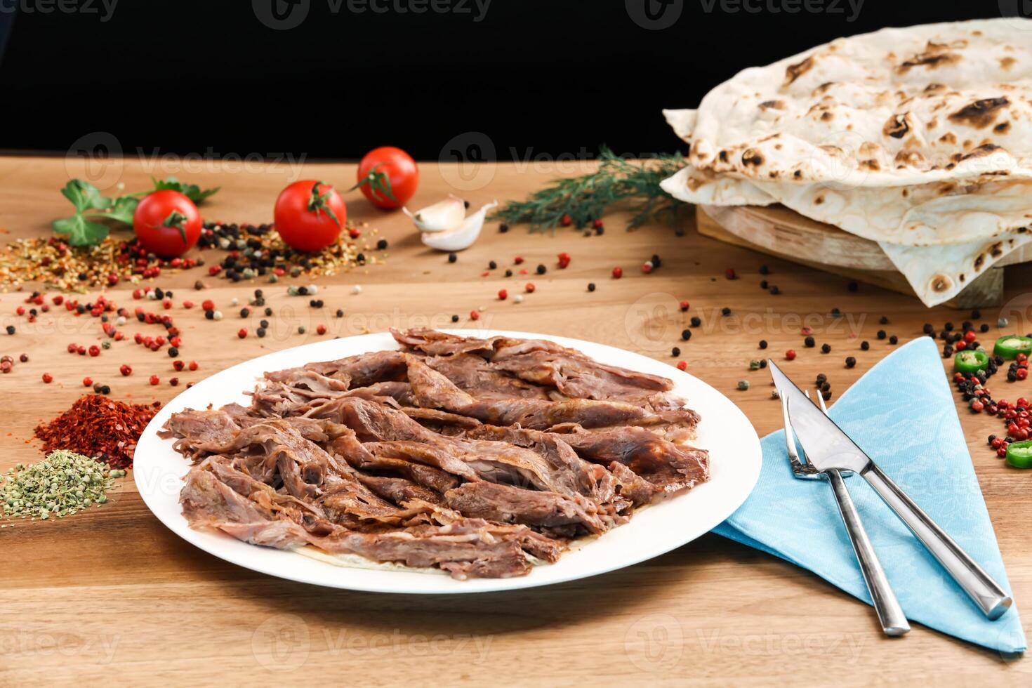 Portion Doner kebab meat served in plate with Pita Bread, knife, fork and tomato isolated on wooden background side view of arabic and turkish fast food photo