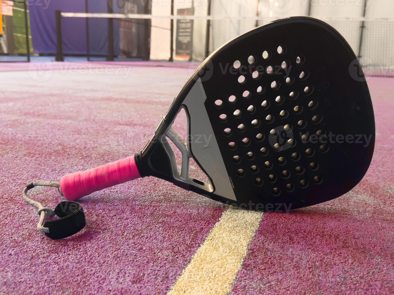 Photo of an orange padel racket and a ball on the ground of a blue outdoor court. Padel concept. Paddle equipment.
