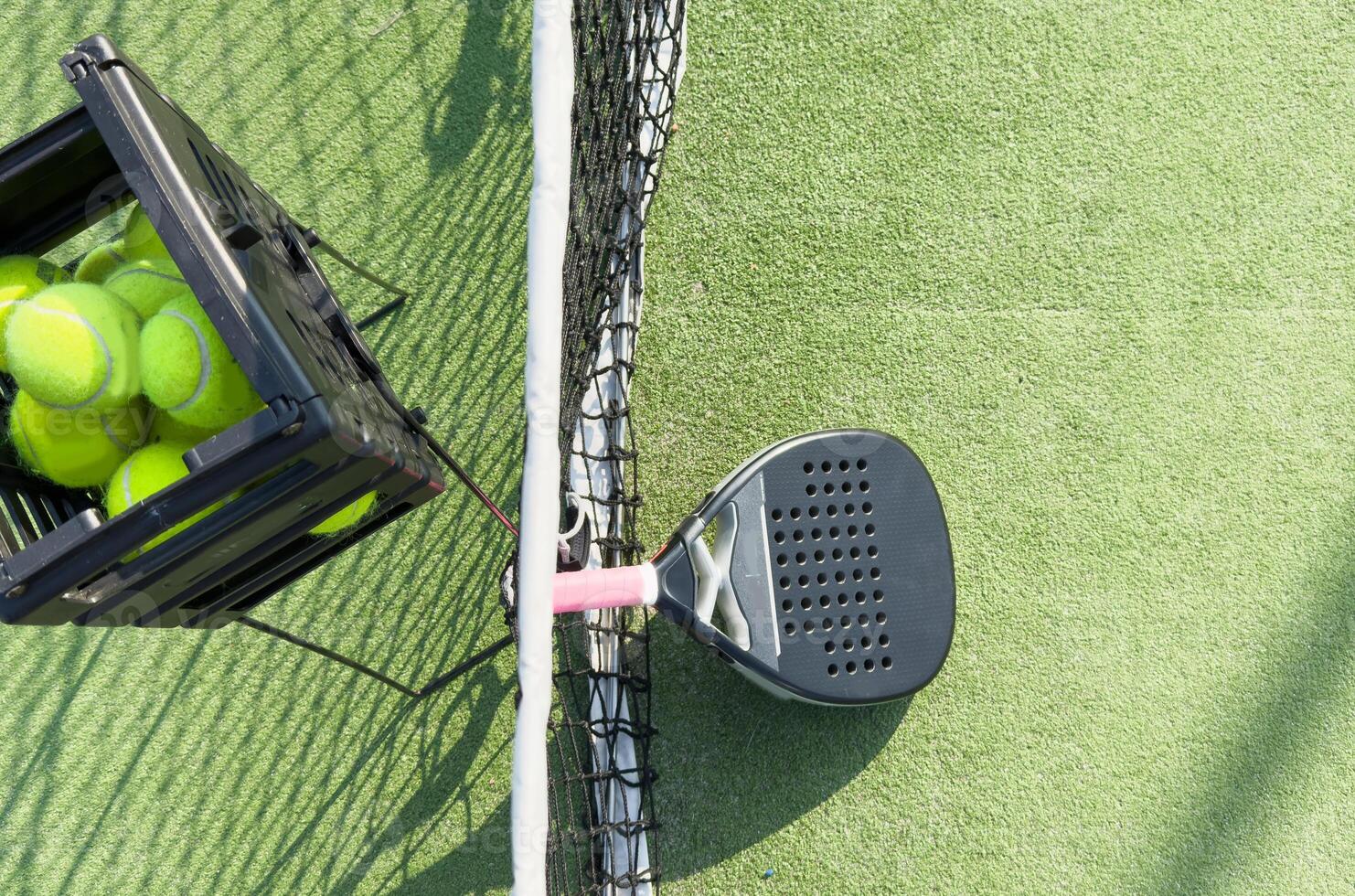 padel racket and yellow balls placed on court near net on sunny day photo