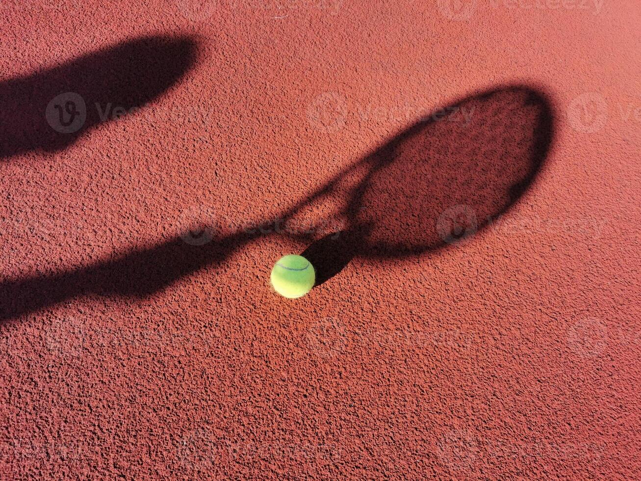 High angle of yellow ball placed on court and covered with shadow of crop person holding padel racket photo