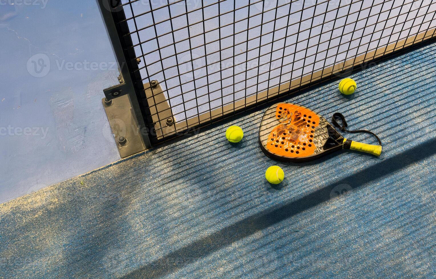 padel racket and yellow balls placed on court near net photo