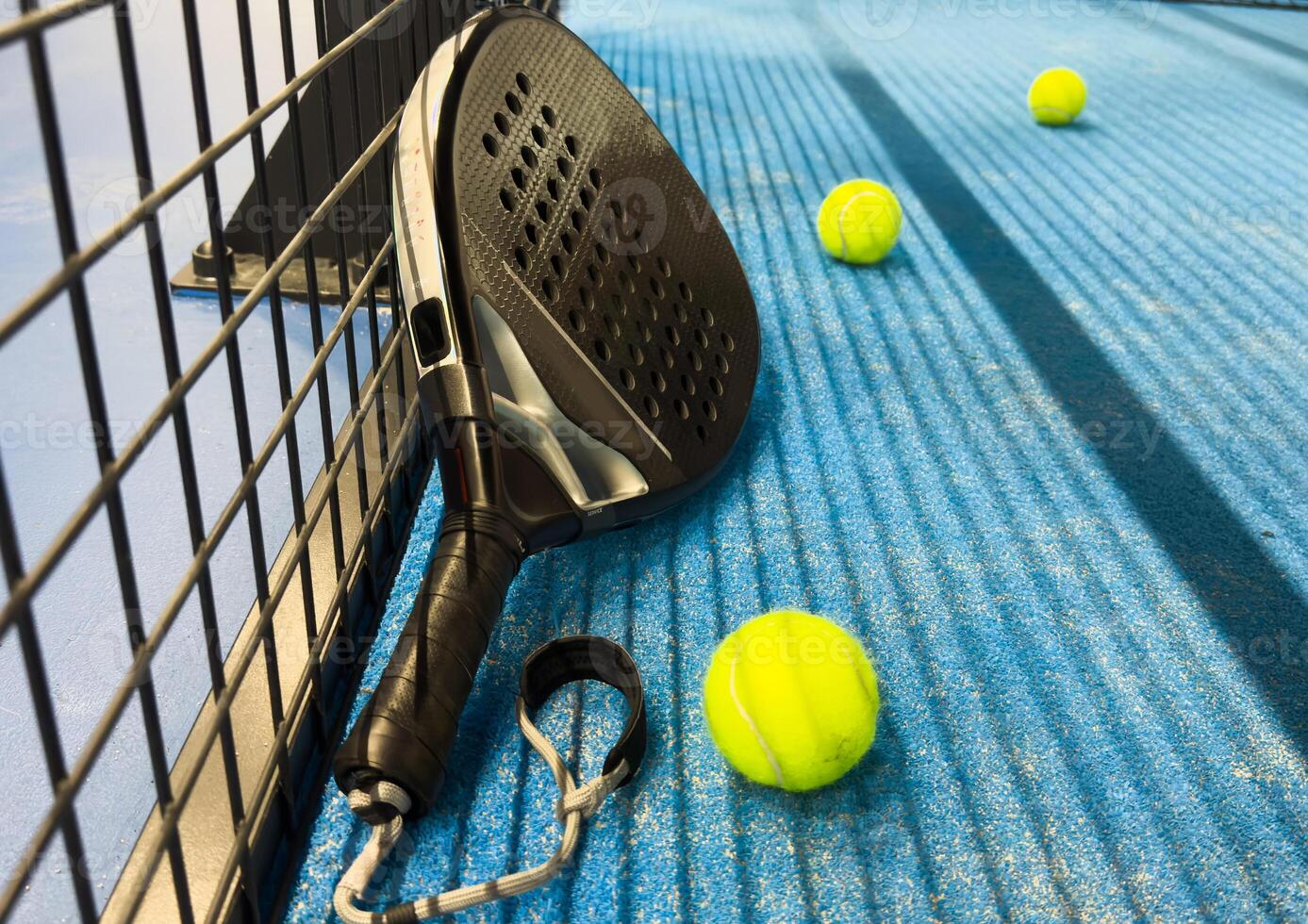 Padel racket and yellow ball behind net on a green court grass turf outdoors at sunset. Paddle is a racquet game. Professional sport concept with space for text photo