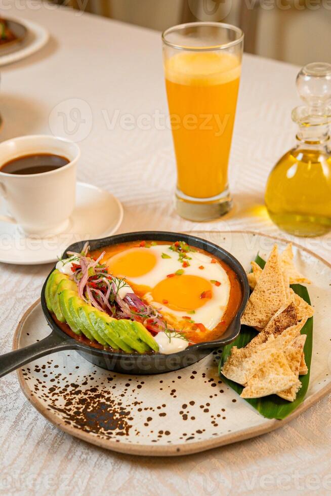 Breakfast with a casserole of sunny-side-up eggs, orange juice, fruits, and avocado photo