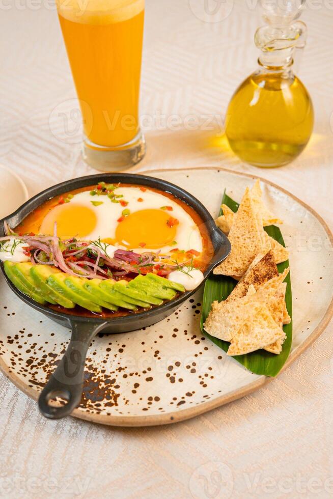 Breakfast with a casserole of sunny-side-up eggs, orange juice, fruits, and avocado photo
