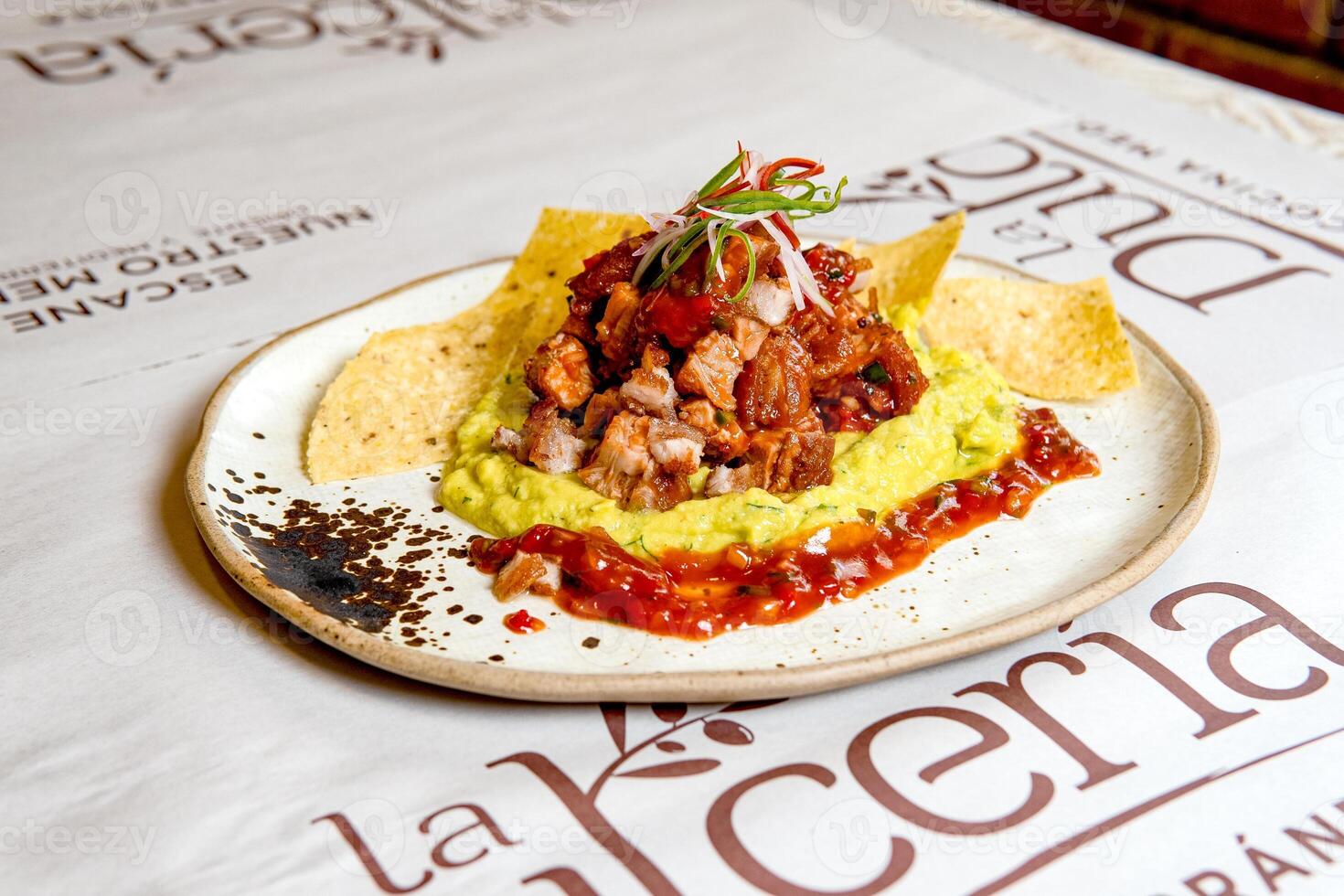 A gourmet dish of crispy pork belly, chicharron, served with guacamole, spicy salsa, and tortilla chips photo