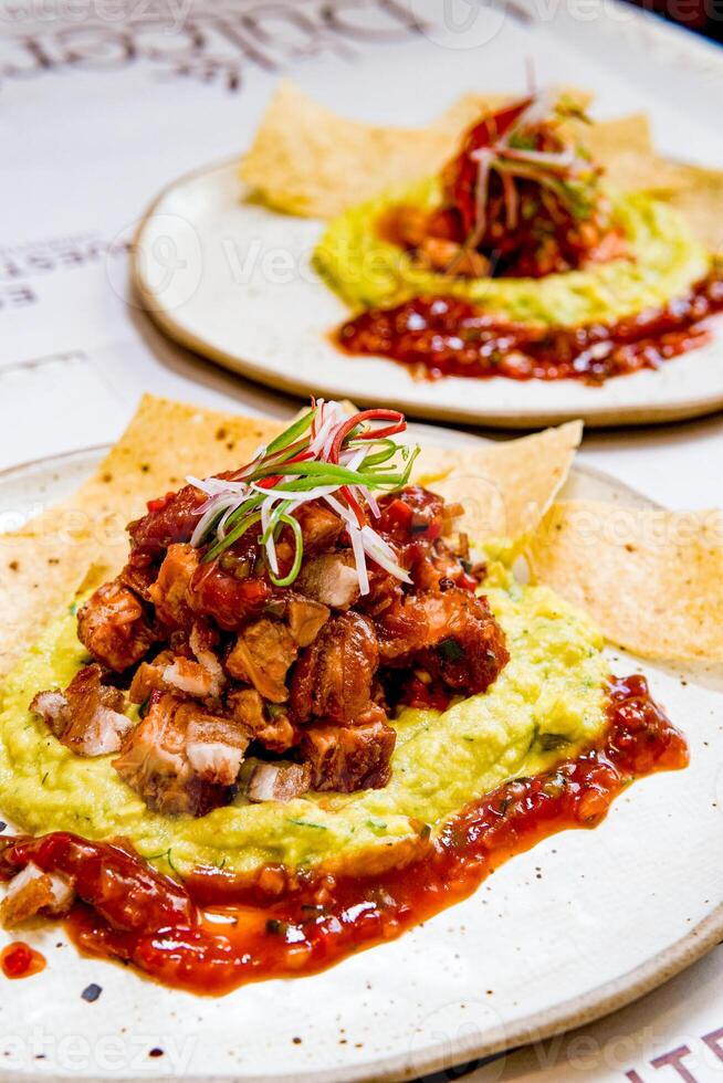 A gourmet dish of crispy pork belly, chicharron, served with guacamole, spicy salsa, and tortilla chips photo