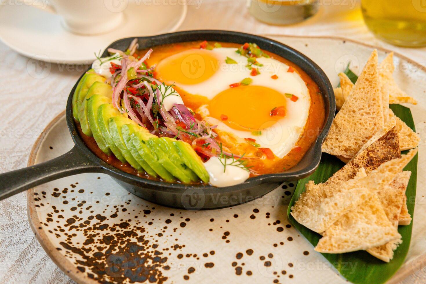 Breakfast with a casserole of sunny-side-up eggs, orange juice, fruits, and avocado photo