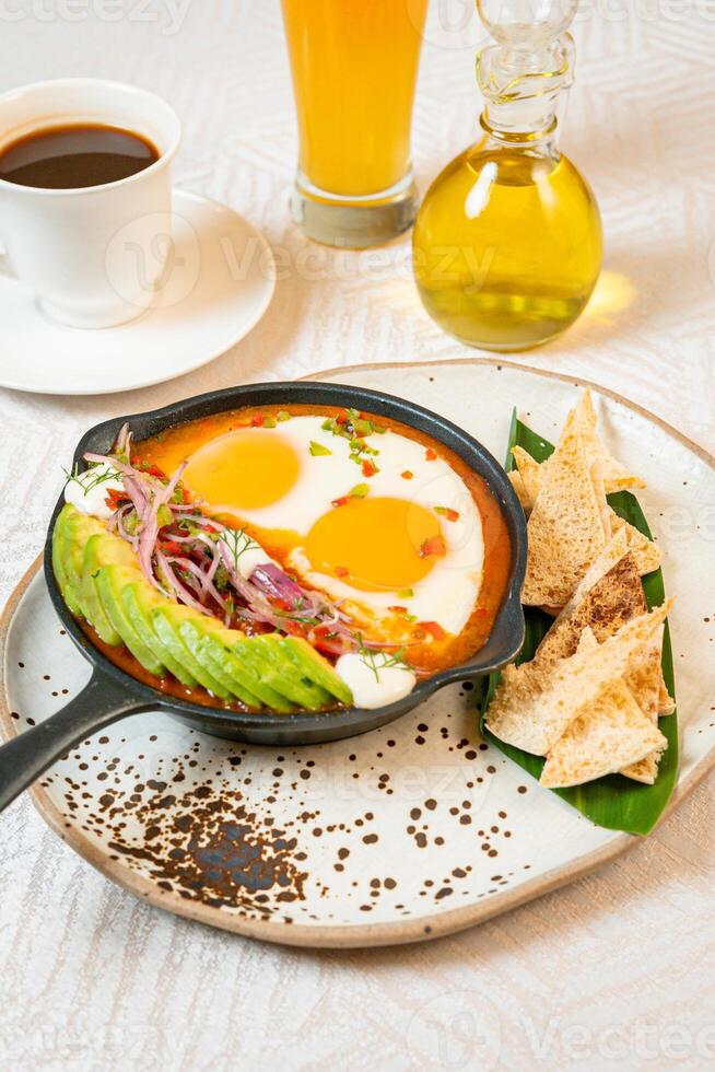 Breakfast with a casserole of sunny-side-up eggs, orange juice, fruits, and avocado photo