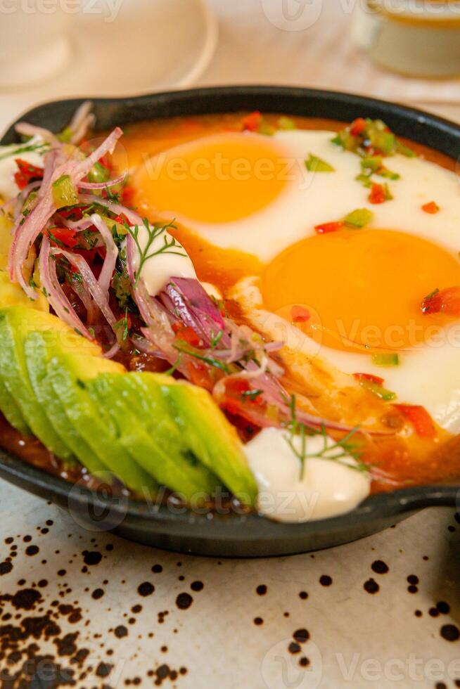 Breakfast with a casserole of sunny-side-up eggs, orange juice, fruits, and avocado photo