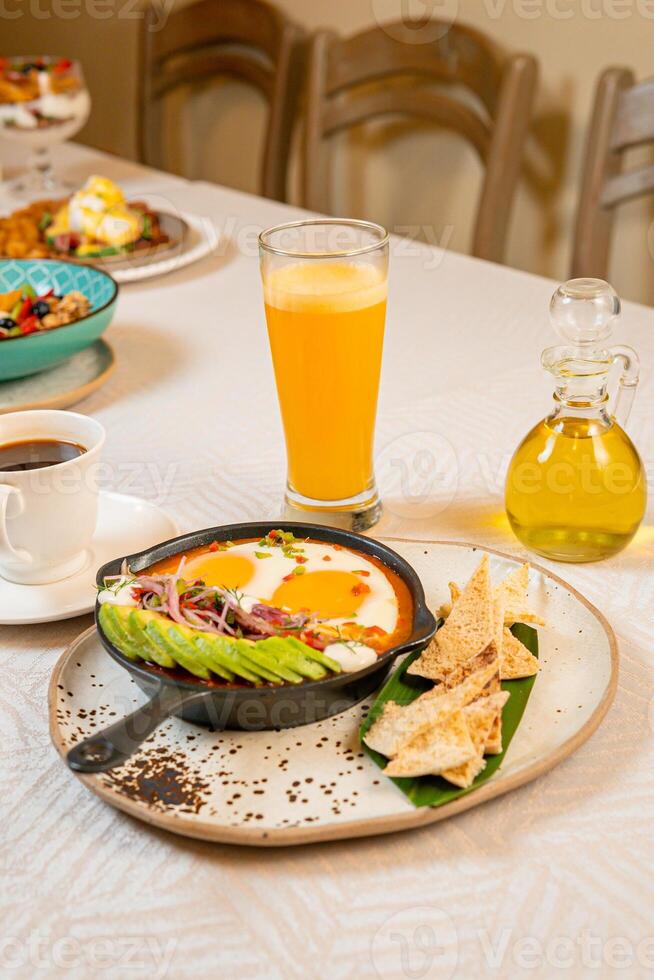 Breakfast with a casserole of sunny-side-up eggs, orange juice, fruits, and avocado photo