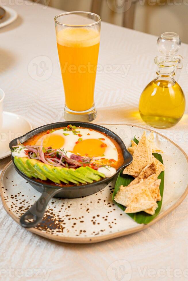 Breakfast with a casserole of sunny-side-up eggs, orange juice, fruits, and avocado photo