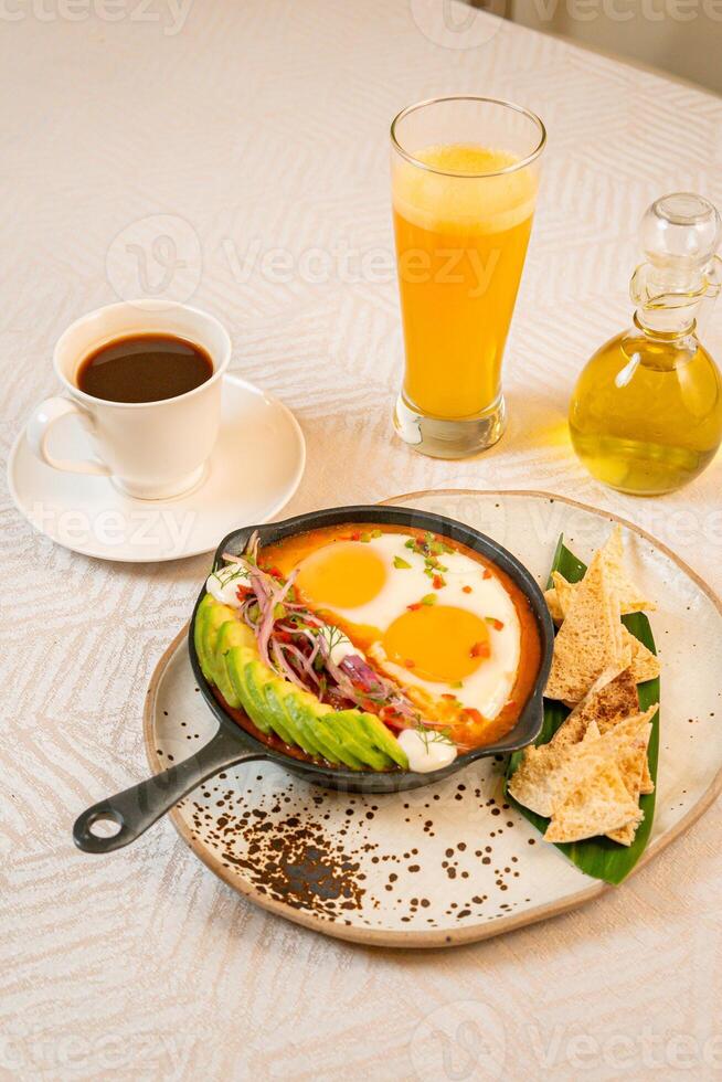 Breakfast with a casserole of sunny-side-up eggs, orange juice, fruits, and avocado photo