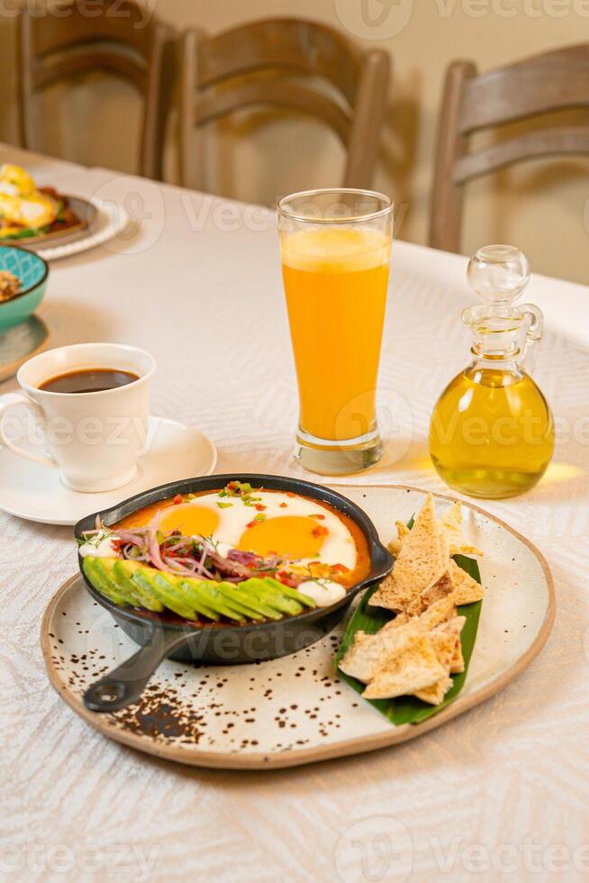Breakfast with a casserole of sunny-side-up eggs, orange juice, fruits, and avocado photo