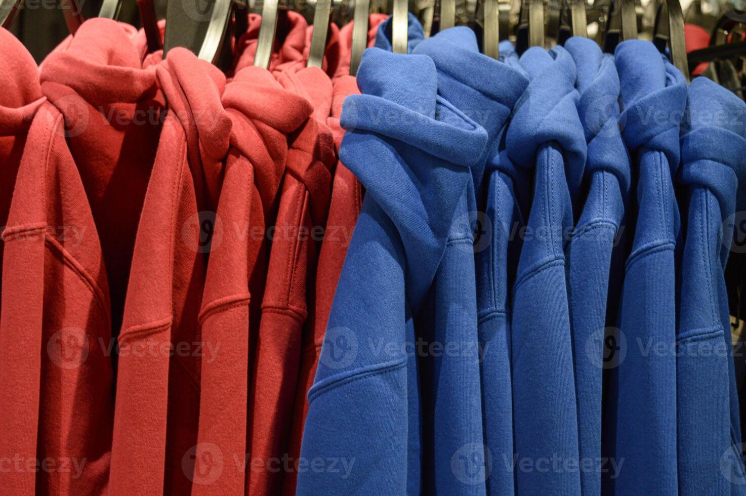 red and blue hoodies are hanging on a hanger many pieces in a row. High quality photo