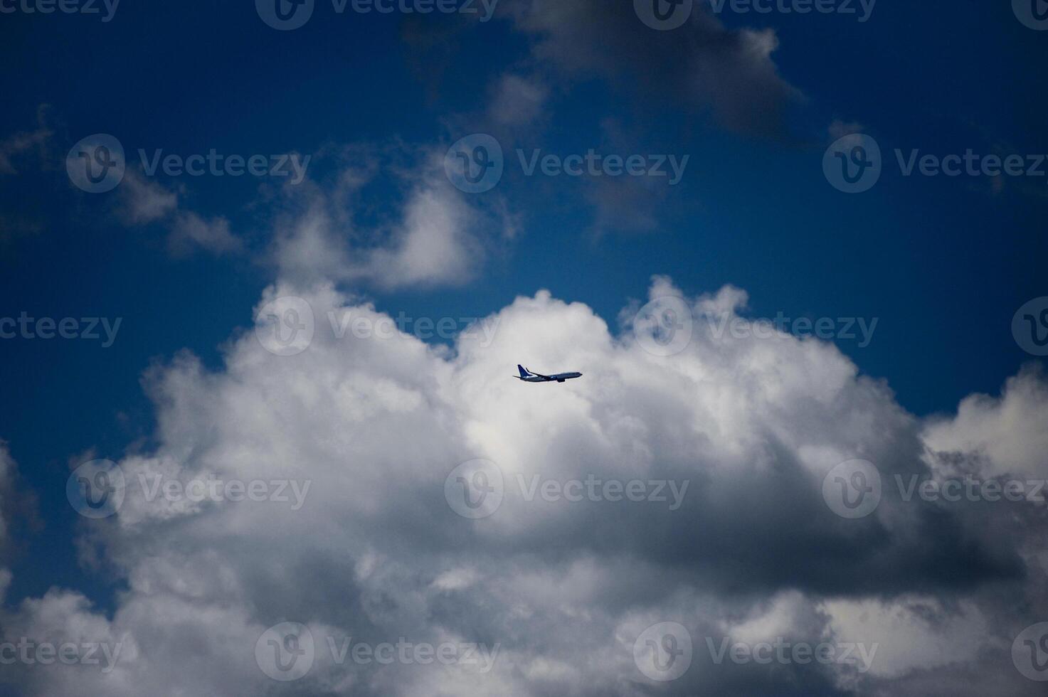 A plane is soaring through the cloudy, vibrant blue sky above photo