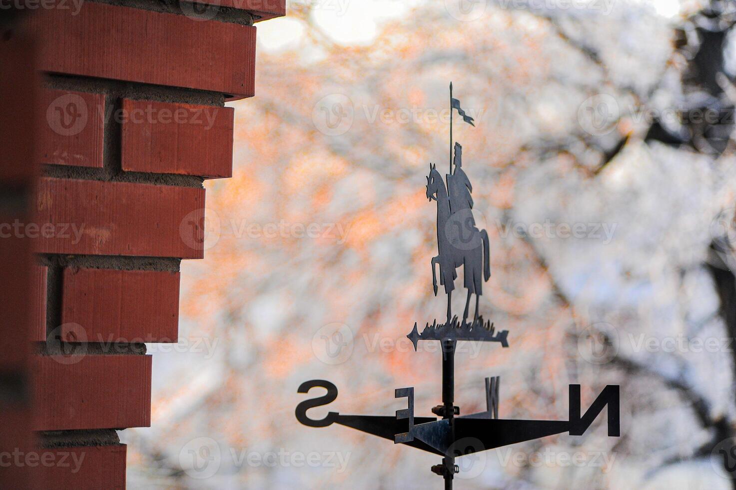 A decorative weather vane featuring a knight is hanging upon a brick wall photo