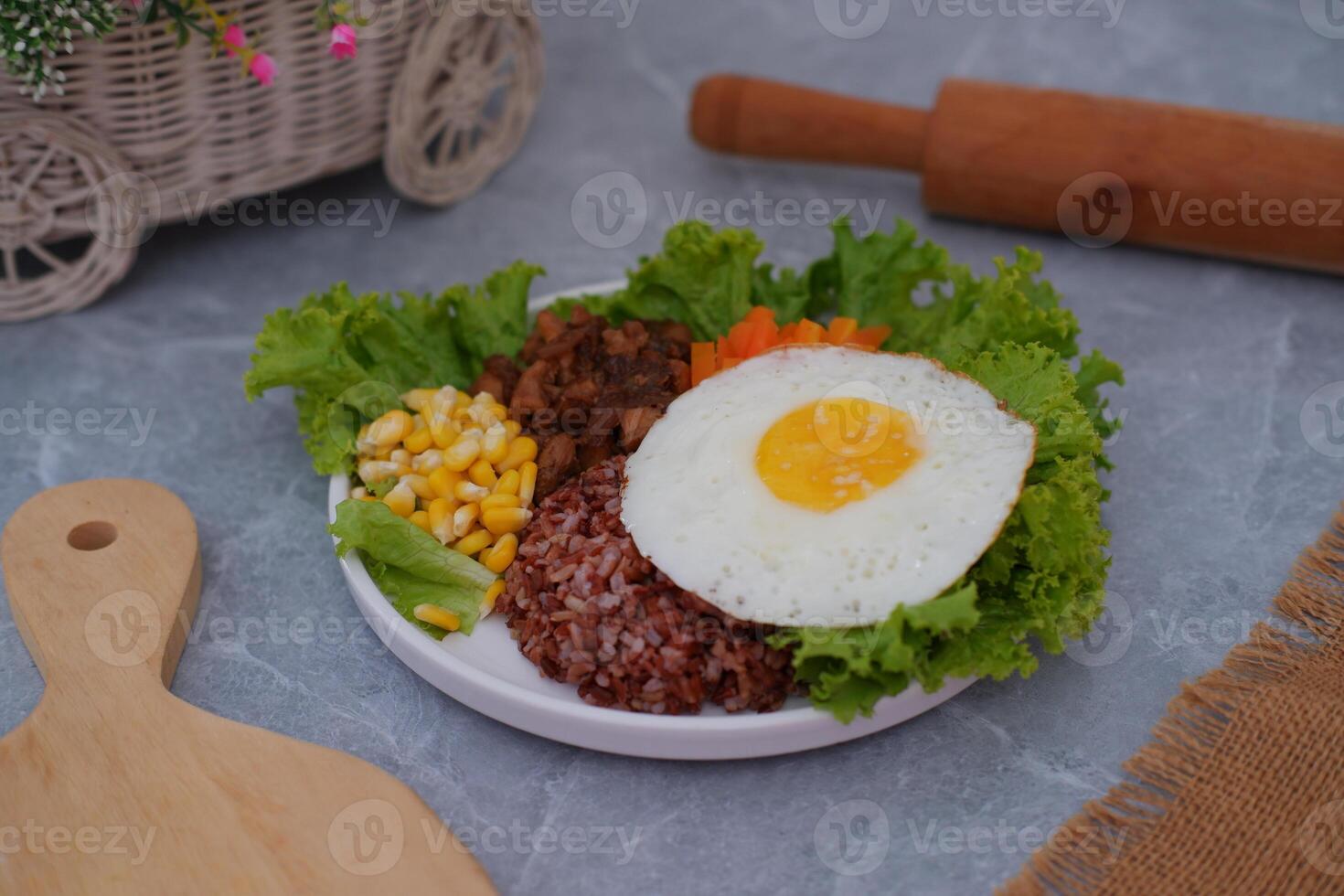 A vibrant meal consisting of red rice, meat, corn, carrots, lettuce, and a sunny side up egg photo