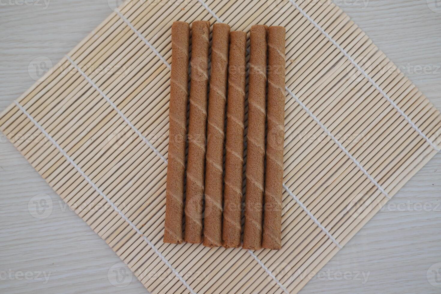 Six chocolate wafer rolls are neatly arranged in a row on a bamboo mat photo