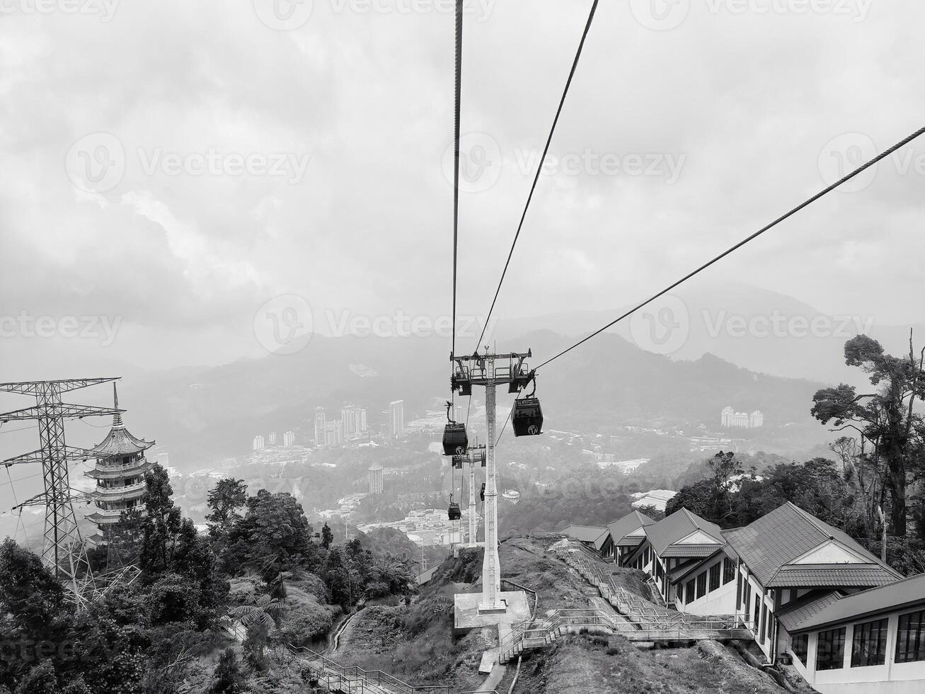 A scenic cable car ride in Malaysia Genting Highland resort reveals a multi tiered pagoda and modern buildings with lush greenery that set in a misty atmosphere. photo