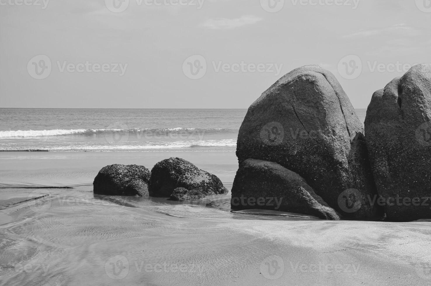 A black and white picturesque beach with golden sand and boulders along the shoreline. photo