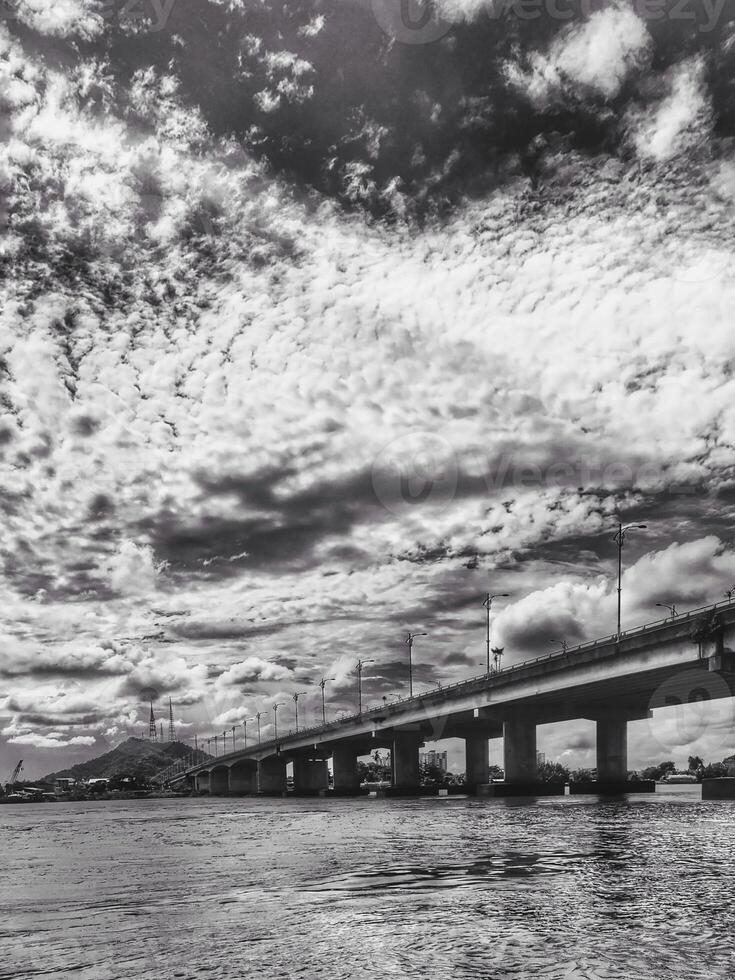 A black and white photograph of a bridge over water and set against a cloudy sky that creates a visually atmospheric scene with striking contrasts in Malaysia Terengganu capital. photo