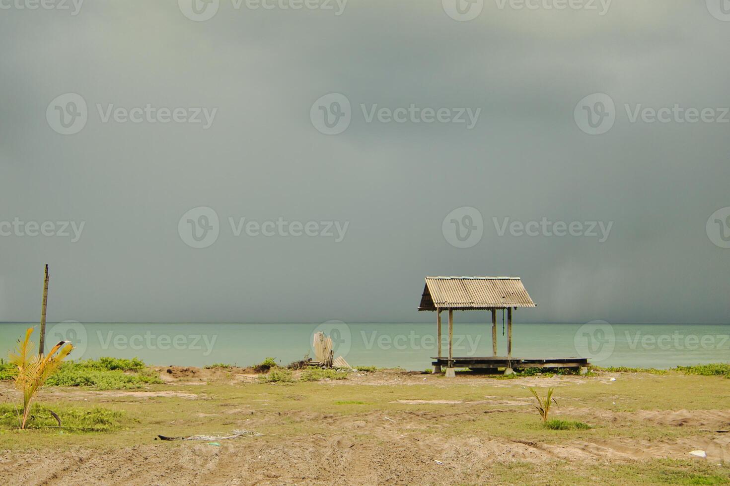 A wooden gazebo by a calm beach surrounded the sea beneath cloudy skies that creates a peaceful setting that embodies simplicity and solitude in the coastal landscape. photo