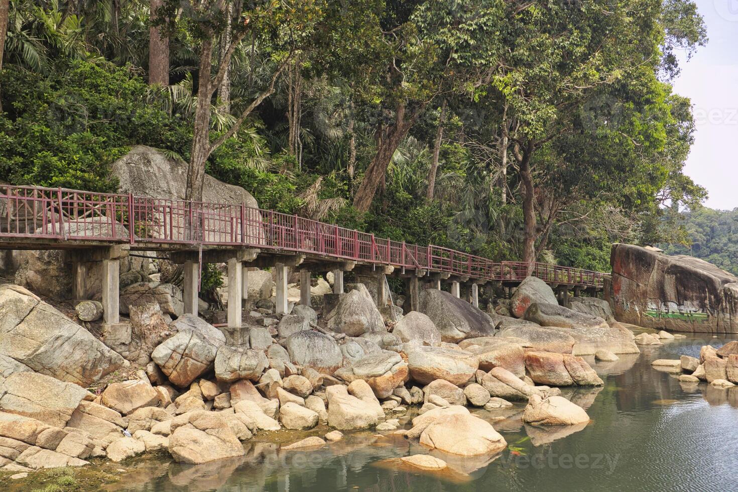 A peaceful trail with a red railing over boulders by a stream near Teluk Cempedak beach. photo