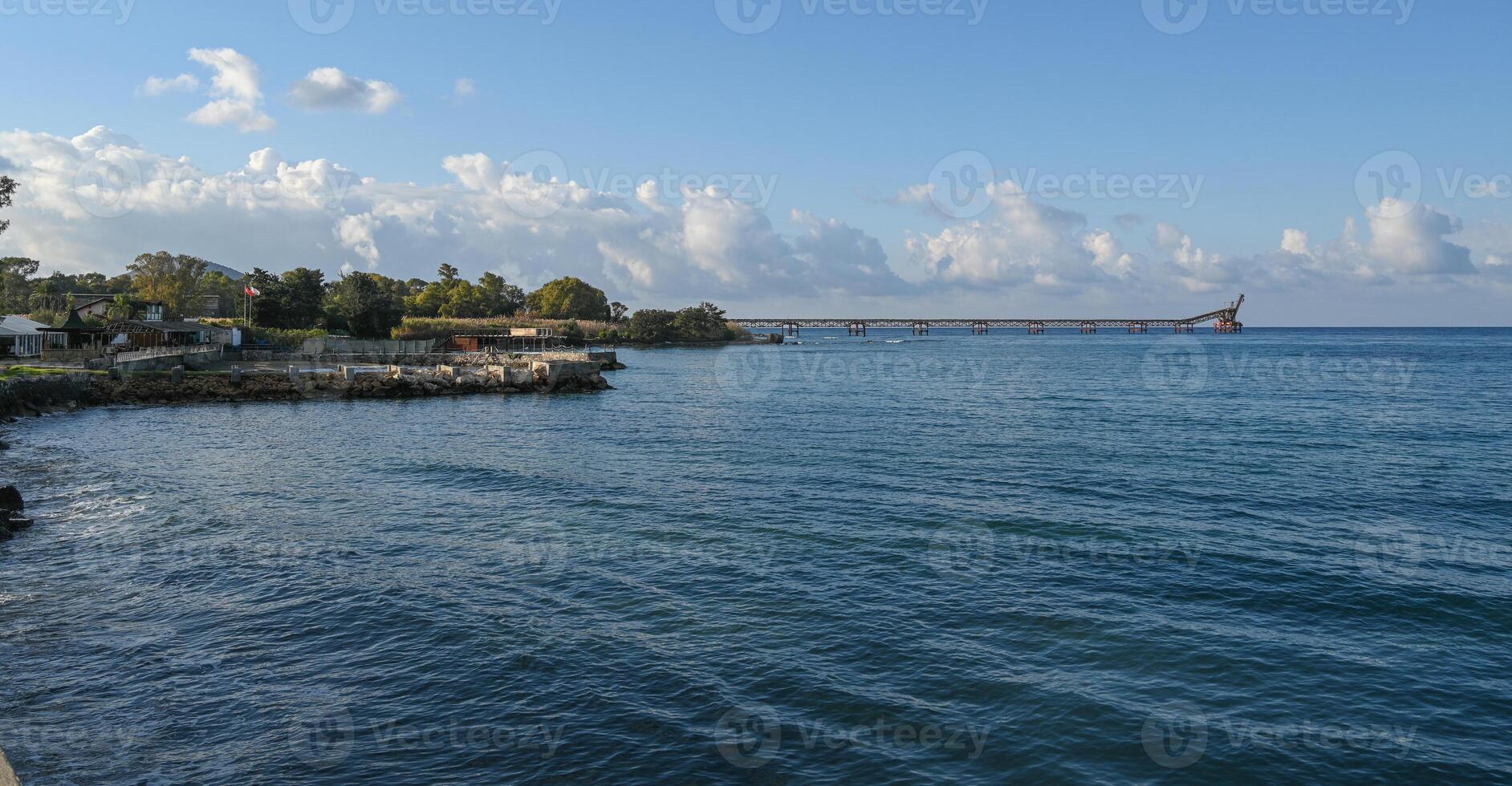 Serene coastal view with a distant pier under a clear blue sky during early afternoon light photo