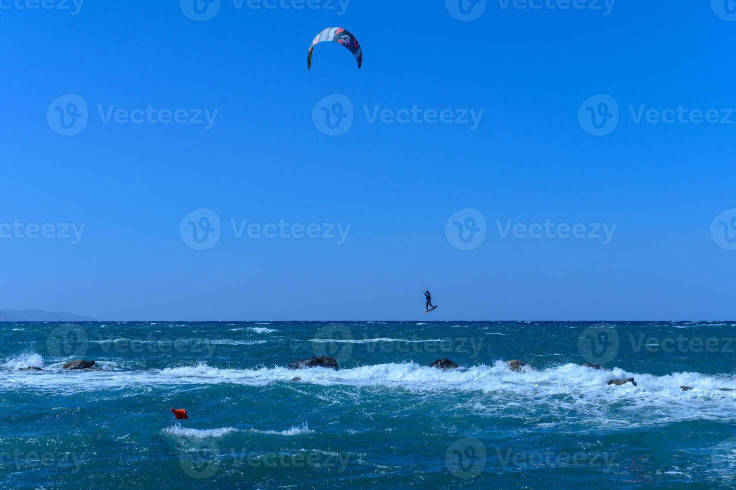Kite surfer glides above vibrant ocean waves under a clear sky during a sunny day photo