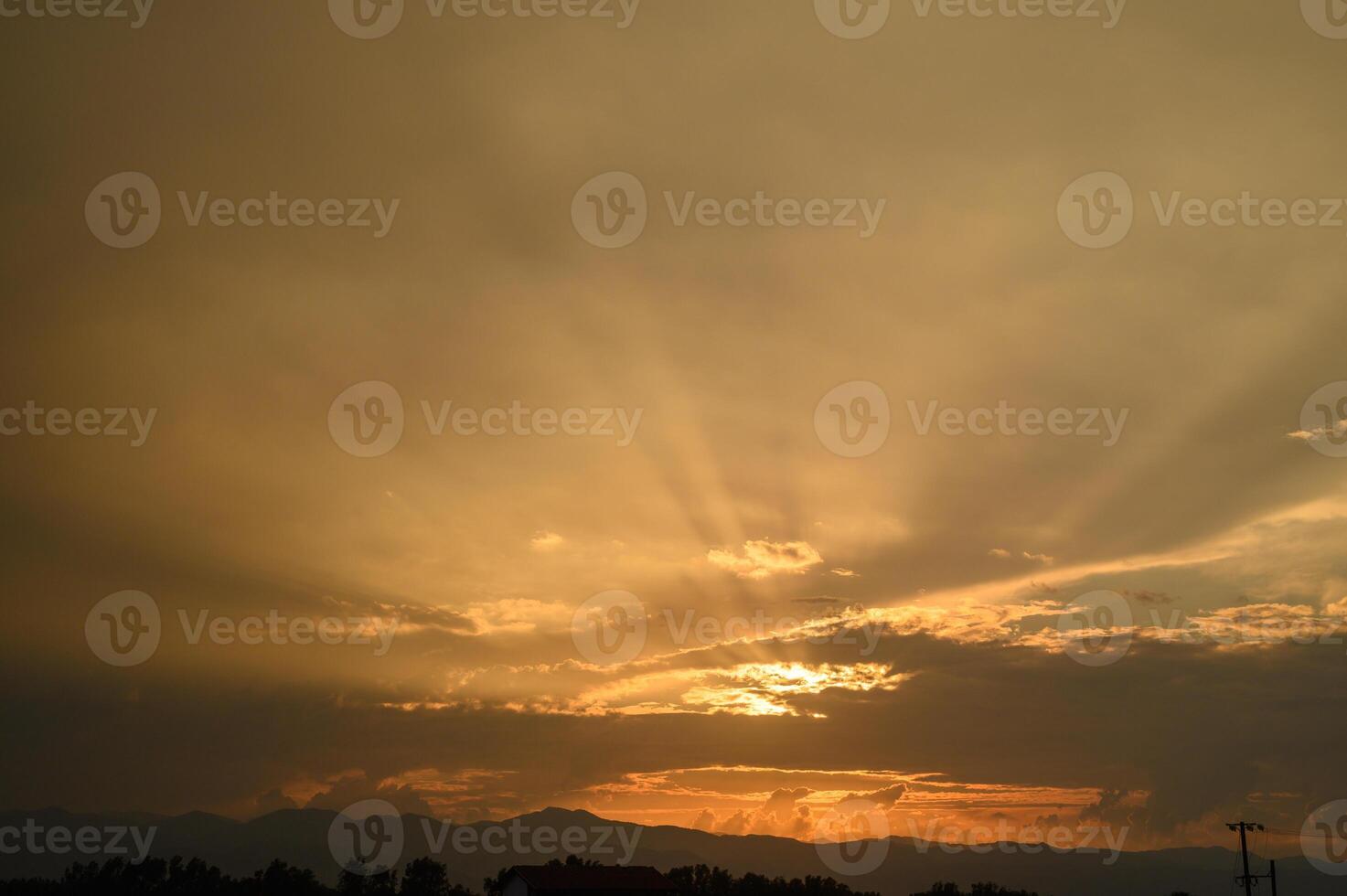 Golden rays break through clouds at sunset over the mountains, creating a serene evening atmosphere photo