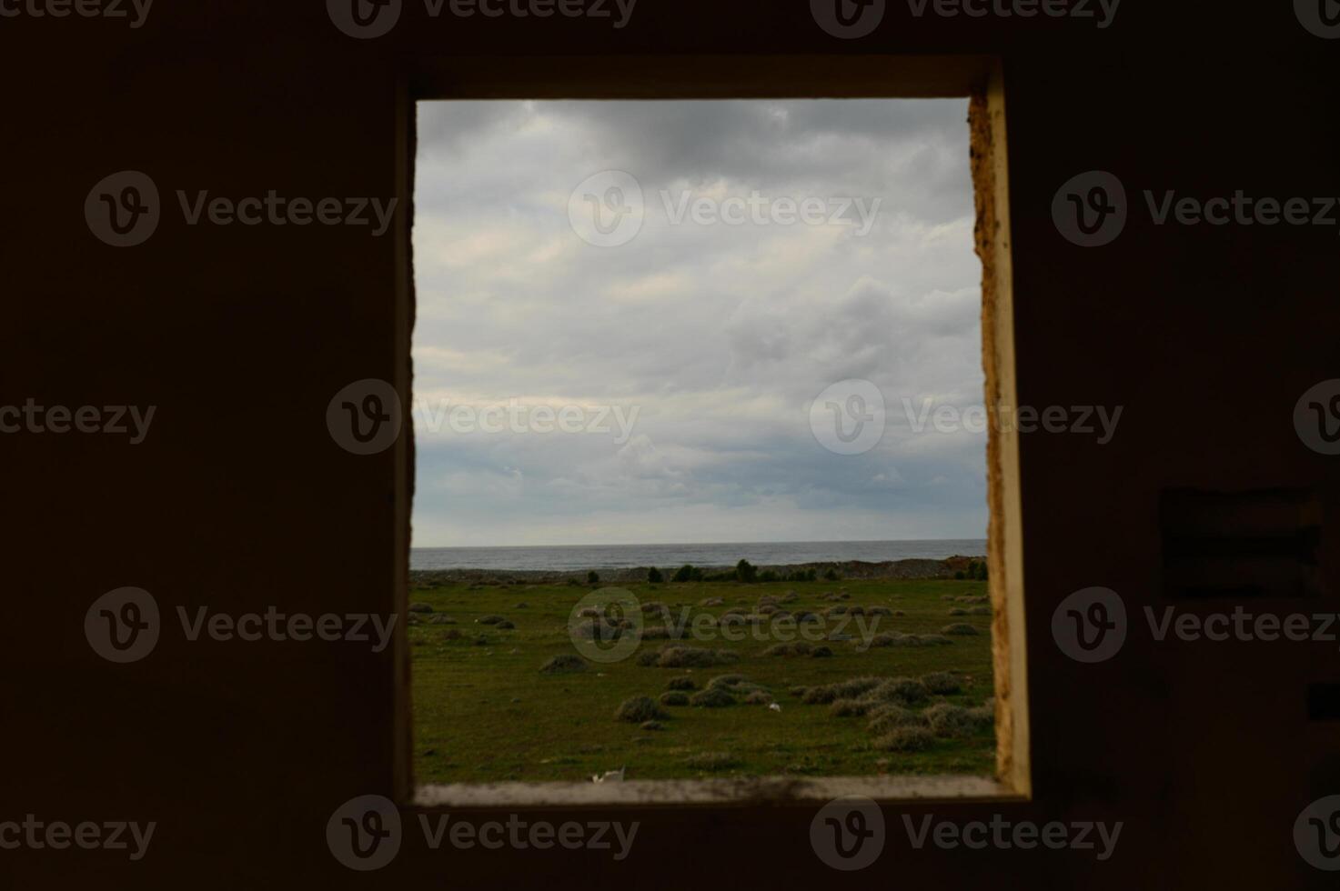 View through an open window showcasing a tranquil landscape by the sea under a moody sky photo