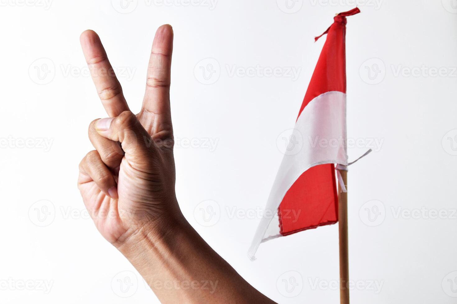 A man's hand raises two fingers sign in front of the red and white flag photo