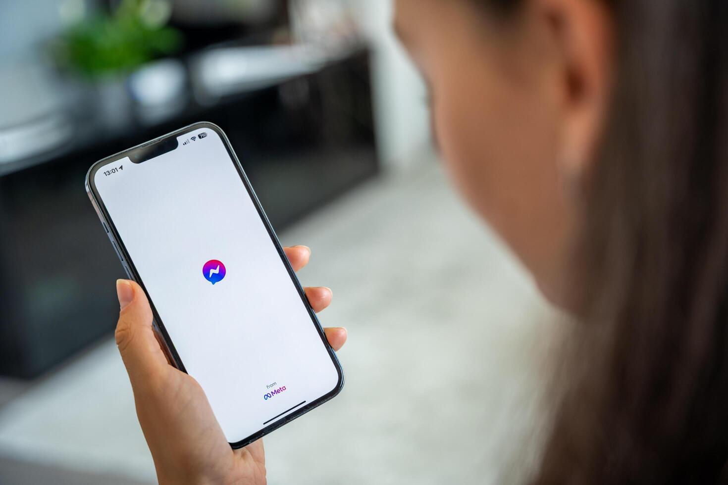 Prague, Czech republic - May 2, 2024. Woman holding iPhone with logo of application Messenger of Meta Facebook on the screen, using mobile application for business home. High quality photo