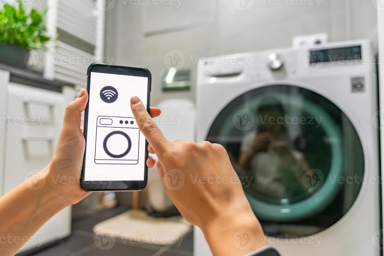 Young woman using mobile phone control via wi-fi and app for washing machine in home. Homesmart and new technology concept. High quality photo
