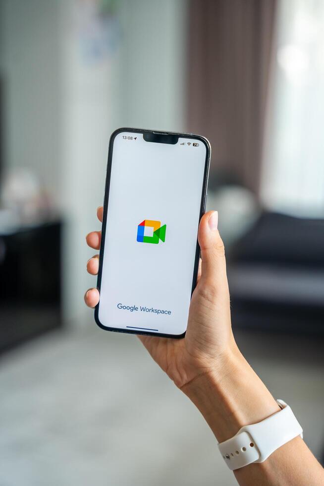 Prague, Czech republic - May 2, 2024. Woman holding iPhone with logo of application Goole Meet on the screen, using mobile application for business home. High quality photo