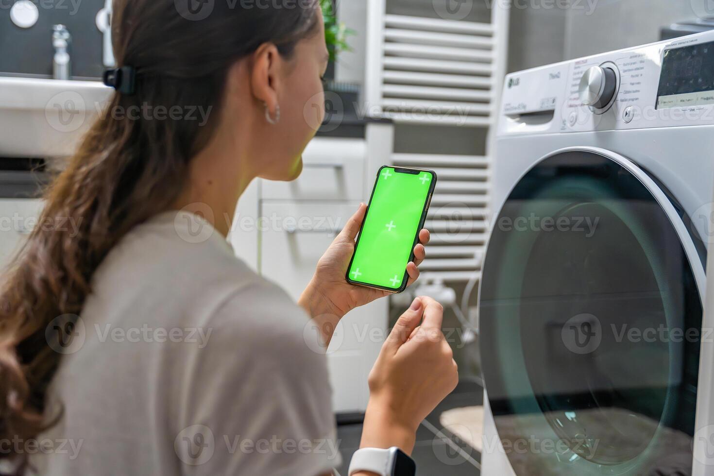 Young woman using mobile phone control via wi-fi and app for washing machine in home. Homesmart app, chroma key green screen. High quality photo