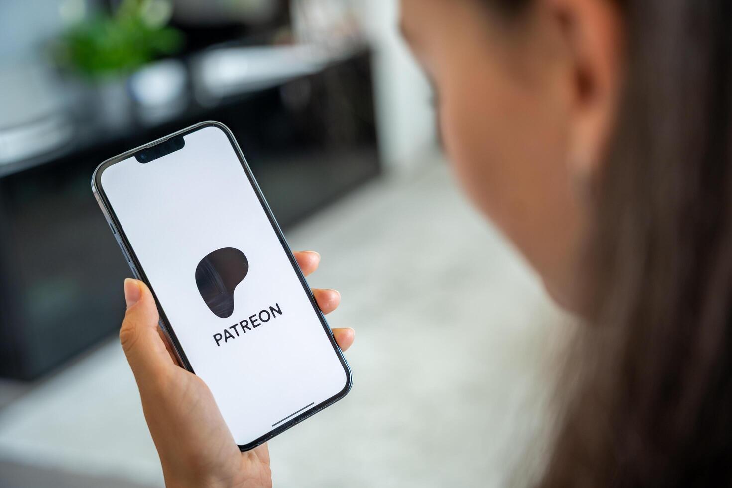 Prague, Czech republic - May 2, 2024. Woman holding iPhone with logo of application Patreon on the screen, using mobile application for business home. High quality photo