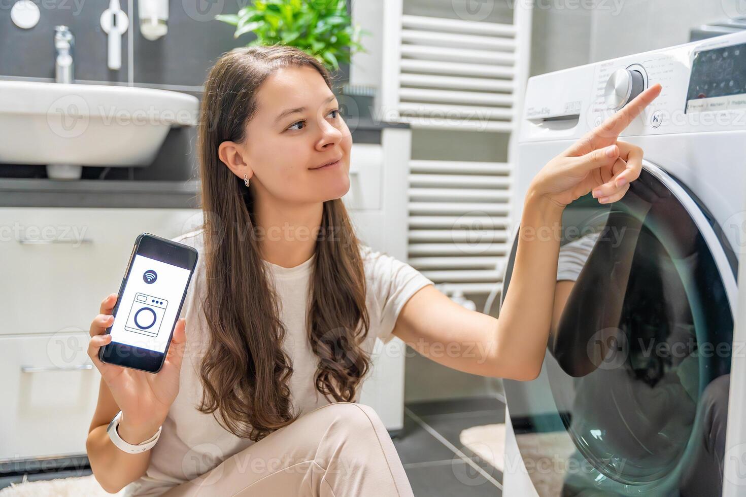 Young woman using mobile phone control via wi-fi and app for washing machine in home. Homesmart and new technology concept. High quality photo