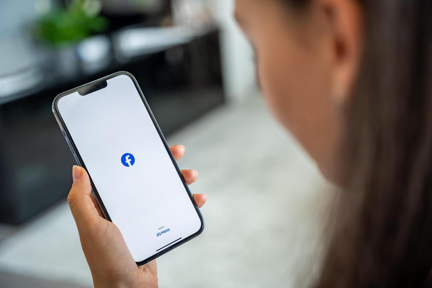 Prague, Czech republic - May 2, 2024. Woman holding iPhone with logo of application Meta Facebook on the screen, using mobile application for business home. High quality photo