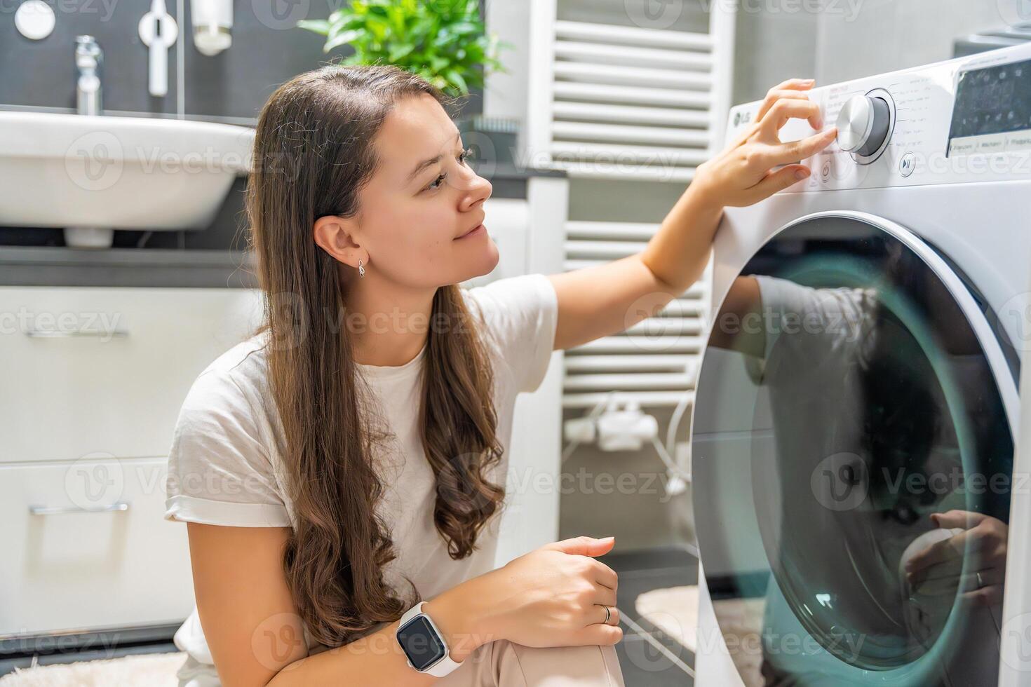 Young woman adjusting washing parameters on washing machine control panel in home bathroom. High quality photo