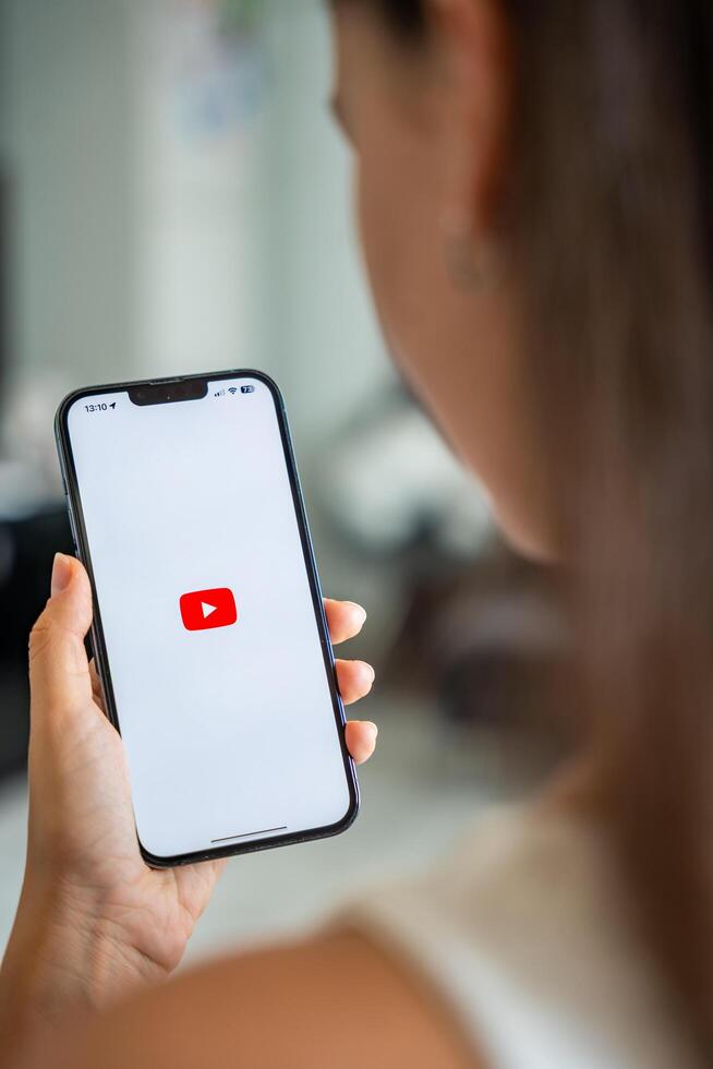 Prague, Czech republic - May 2, 2024. Woman holding iPhone with logo of application YouTube on the screen, using mobile application for business home. High quality photo