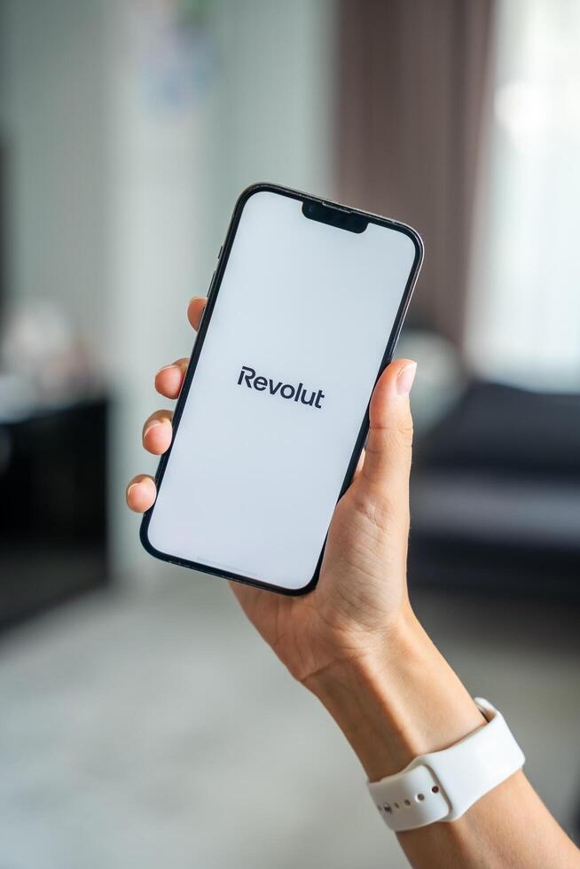 Prague, Czech republic - May 2, 2024. Woman holding iPhone with logo of application Revolute on the screen, using mobile application for business home. High quality photo