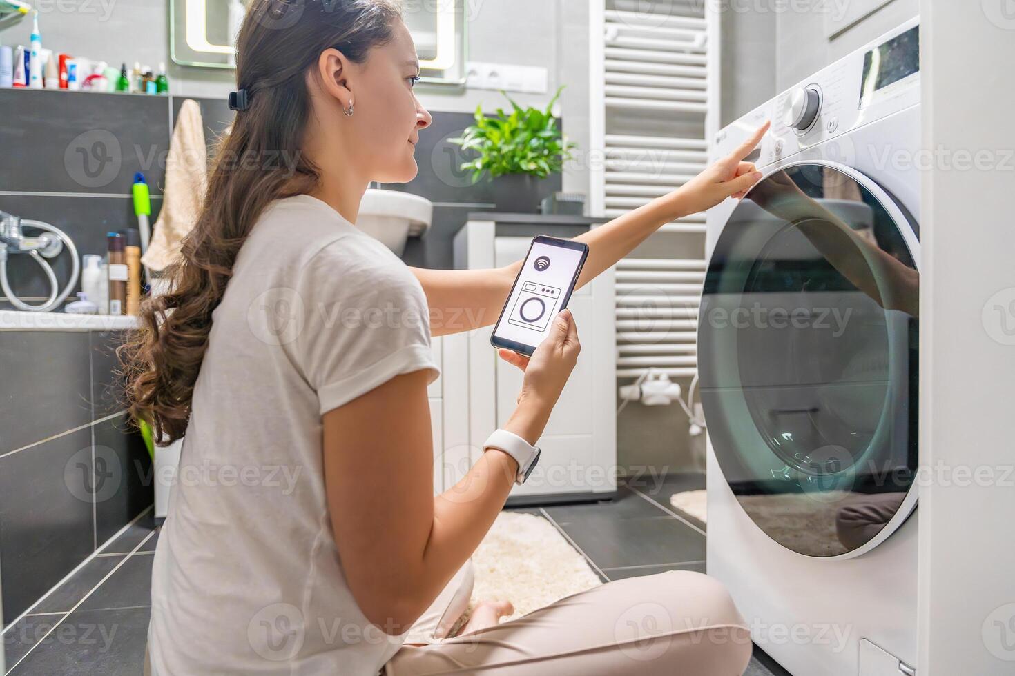 Young woman using mobile phone control via wi-fi and app for washing machine in home. Homesmart and new technology concept. High quality photo