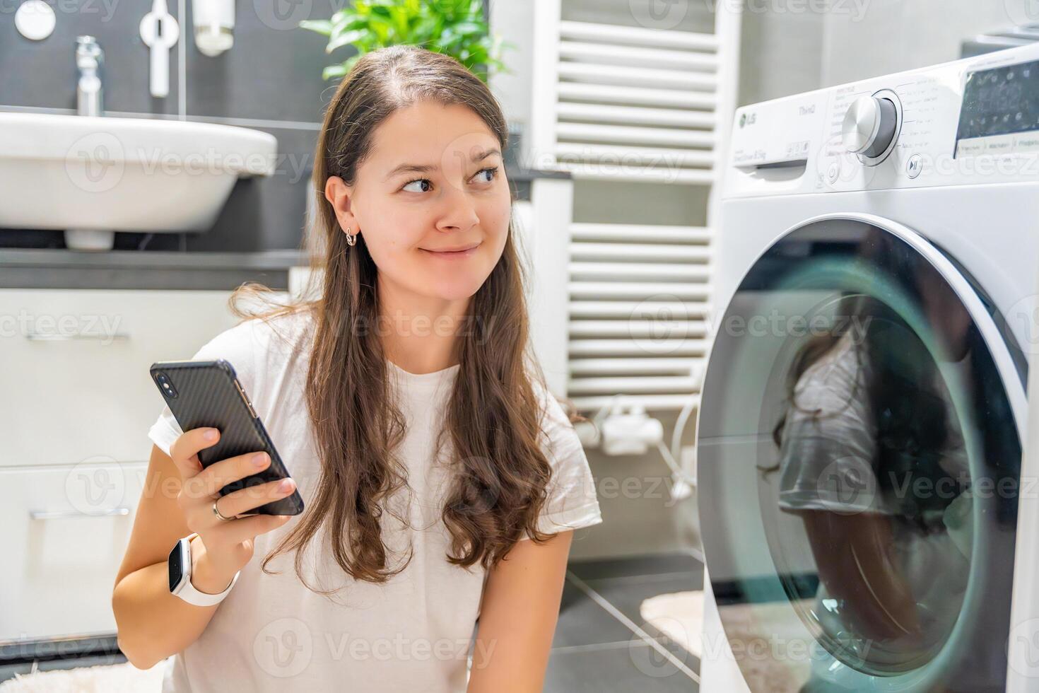 Young woman using mobile phone control via wi-fi and app for washing machine in home. Homesmart and new technology concept. High quality photo