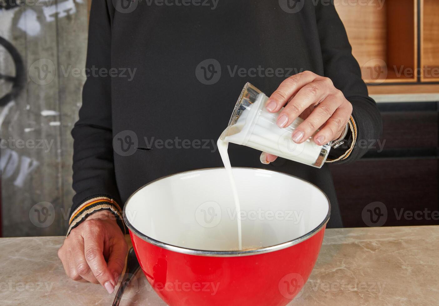 A person adds milk to a red mixing bowl as part of the preparation process for a homemade baking recipe in the kitchen. photo