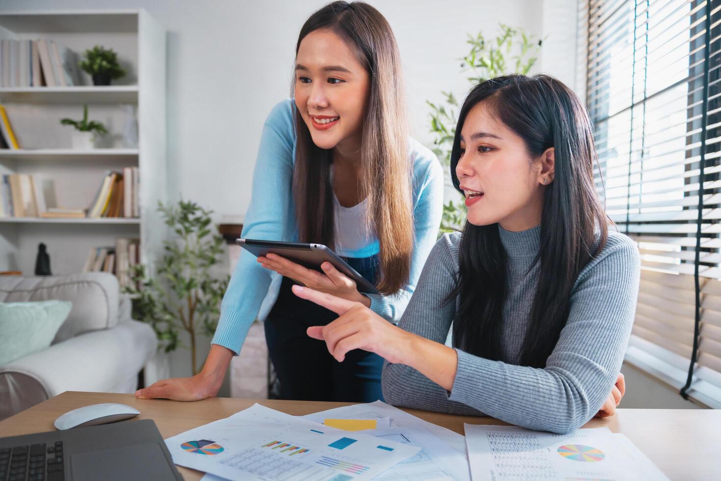 Two women are sitting at a desk looking at a laptop photo