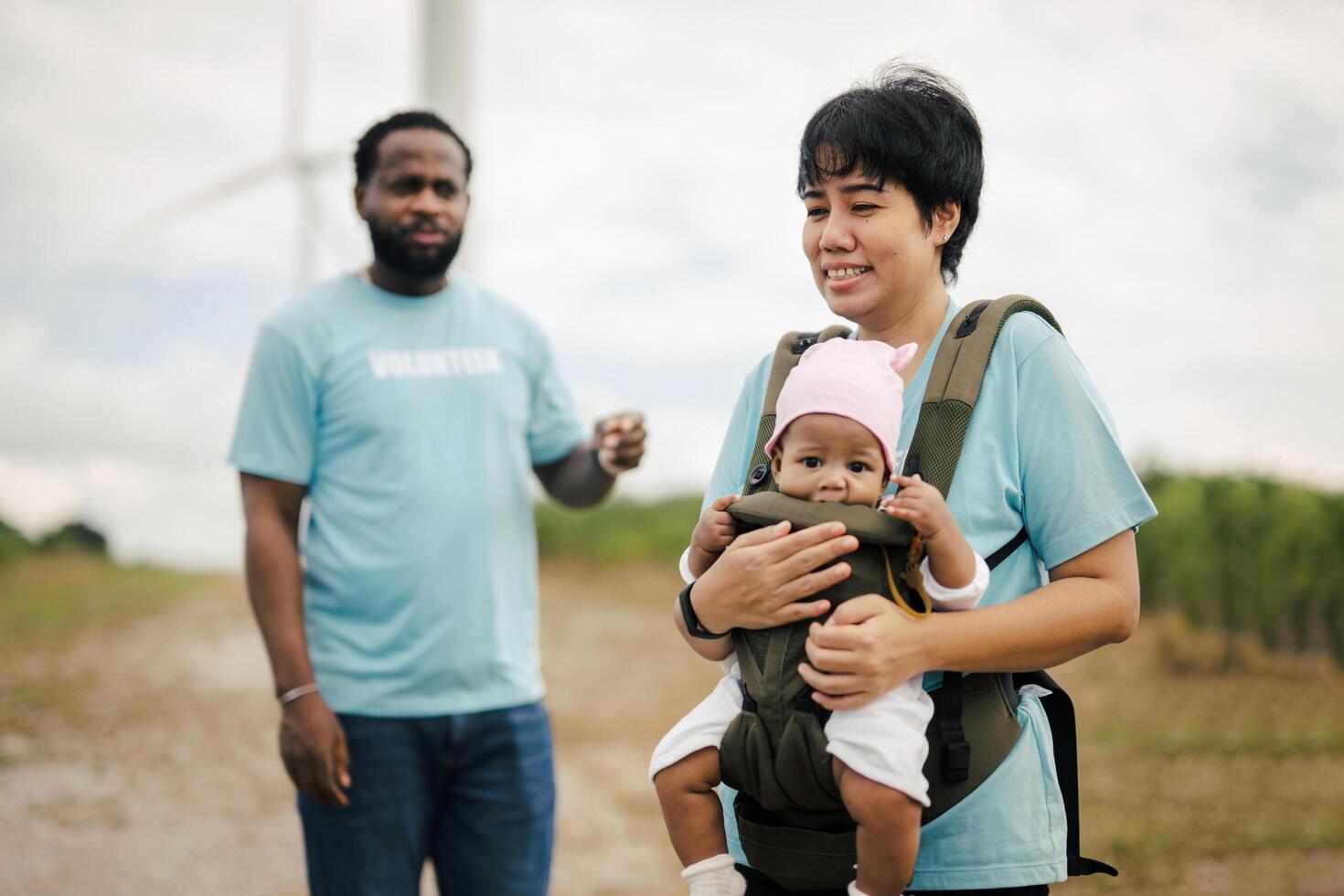 woman is holding a baby in a baby carrier while a man photo
