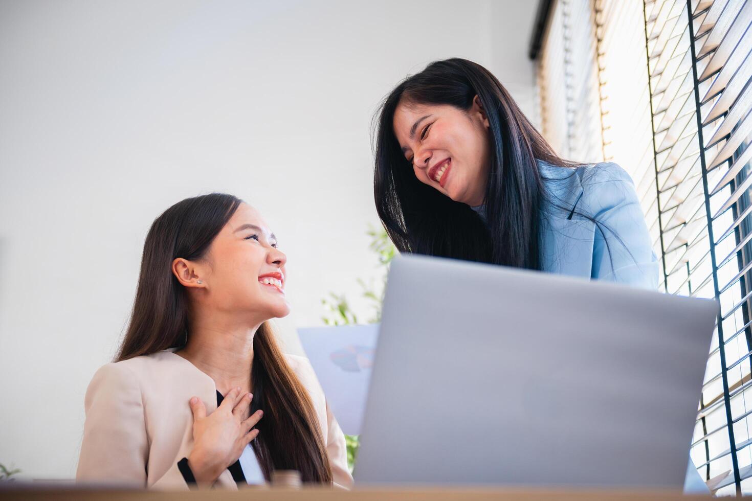 two women are sitting at a desk with a laptop in front of them photo