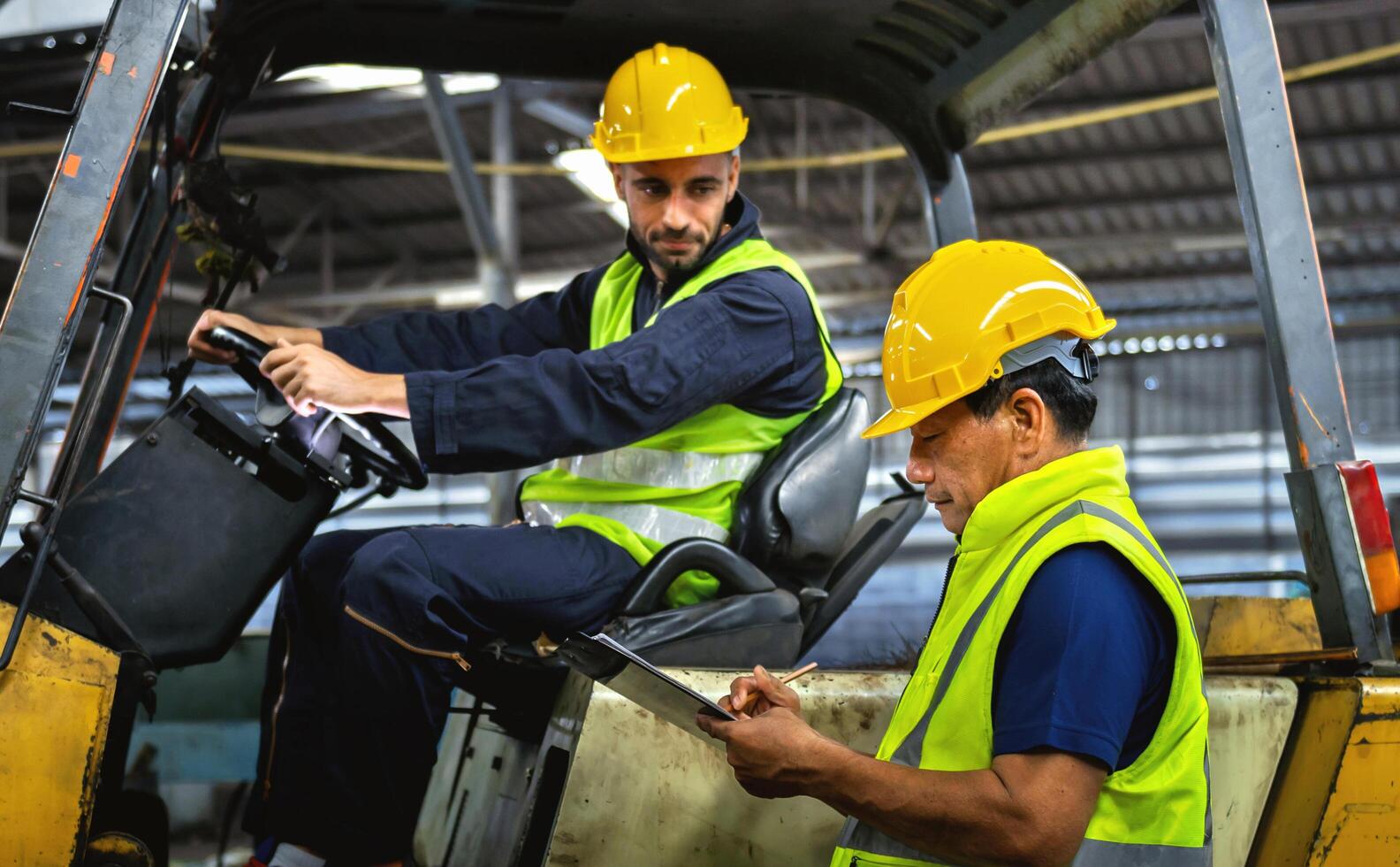 Two men in yellow helmets and safety vests are inspecting a forklift photo
