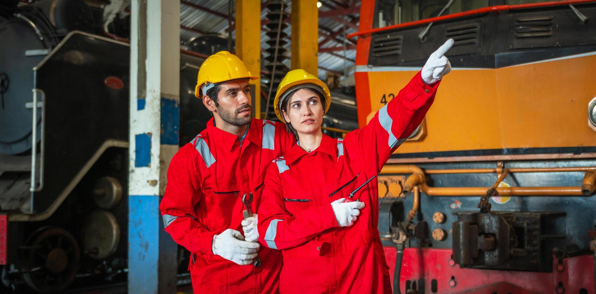 Two workers in red and yellow safety gear pointing at a train photo